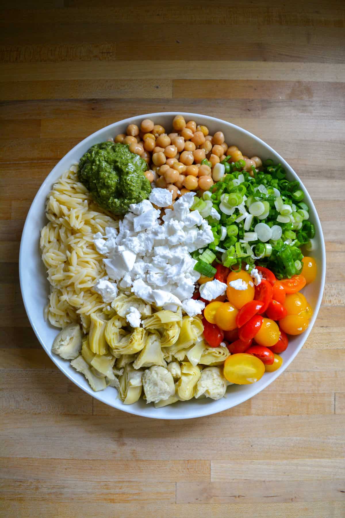 Orzo, tomatoes, chickpeas, artichokes, and feta cheese in a bowl.