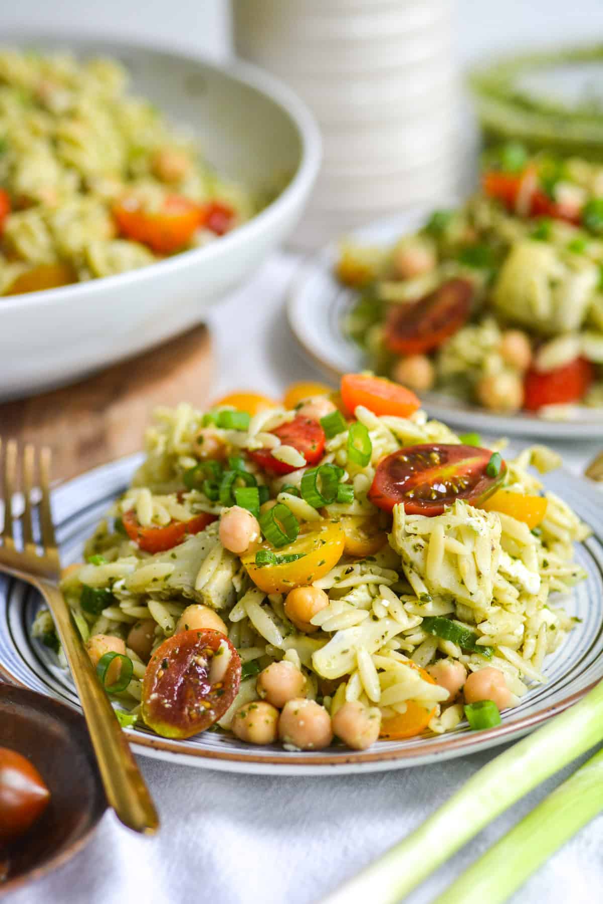 Orzo Pesto Pasta Salad on a plate topped with cherry tomatoes on a small plate.