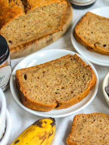 A slice of Vegan Banana Bread on a white plate on a linen coth.