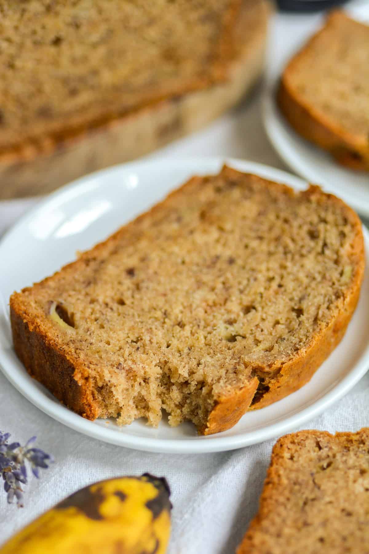 A slice of Vegan Banana Bread with a bite taken out of it on a white plate.