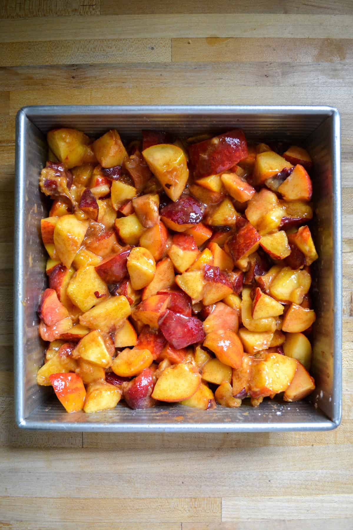 Peach chunks mixed with sugar and cinnamon in a baking dish.