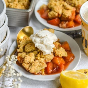 Peach cobbler on a plate topped with a scoop of vanilla ice cream.