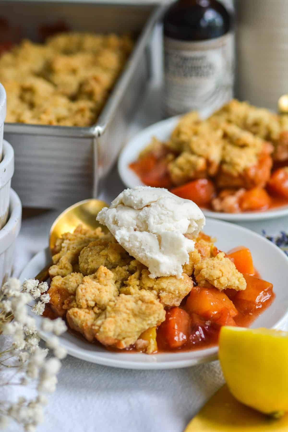 Vegan Peach cobbler on a plate topped with a scoop of vanilla ice cream.