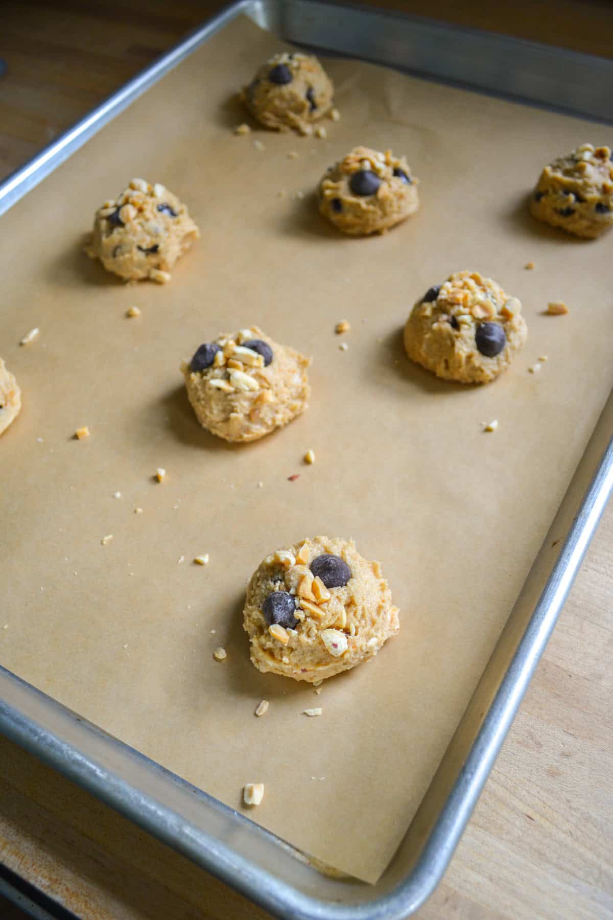 Cookie dough scooped onto a cookie sheet topped with more peanuts and chocolate chips.