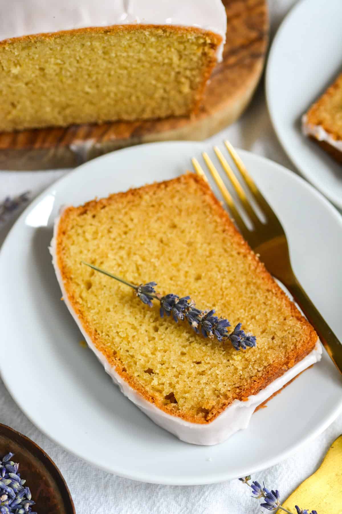 A slice of lemon lavender cake topped with a lavender sprig on a white plate.