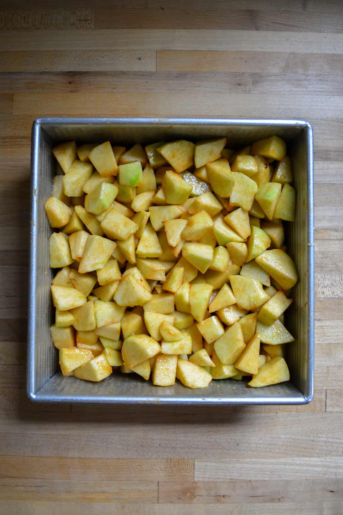 Apples combined with spices in a square pan.