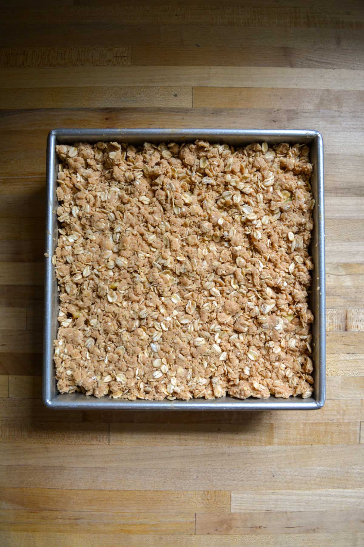 Apples topped with the crumble mixture in a square pan.