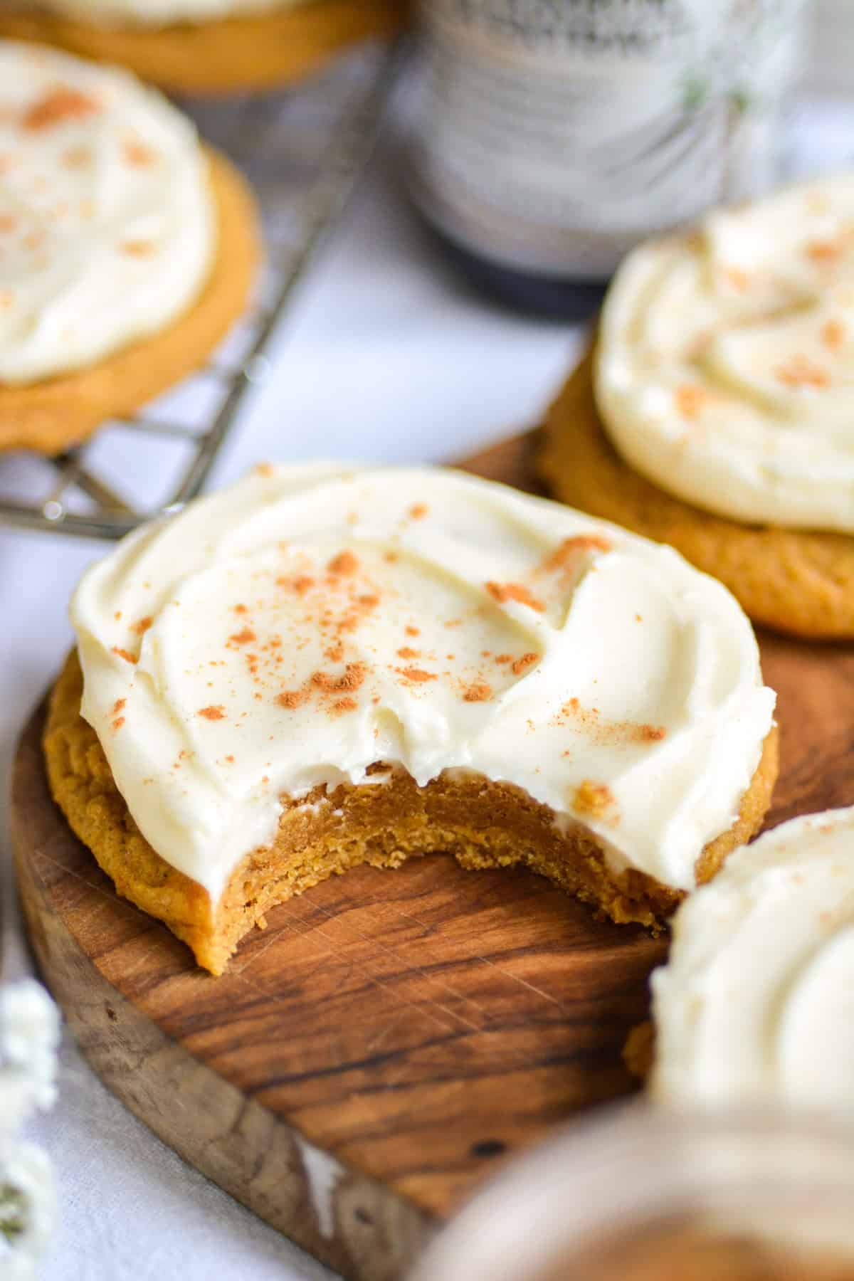 A bite taken out of a vegan iced pumpkin cookie on a wooden board.