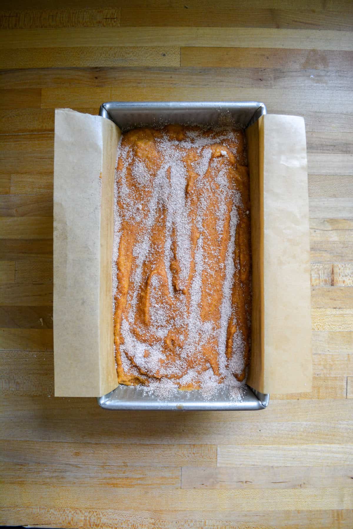 Batter in a loaf pan with cinnamon sugar on top.