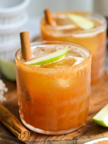 Two Bourbon Whiskey Apple Cider Cocktails in glasses on a wooden board.
