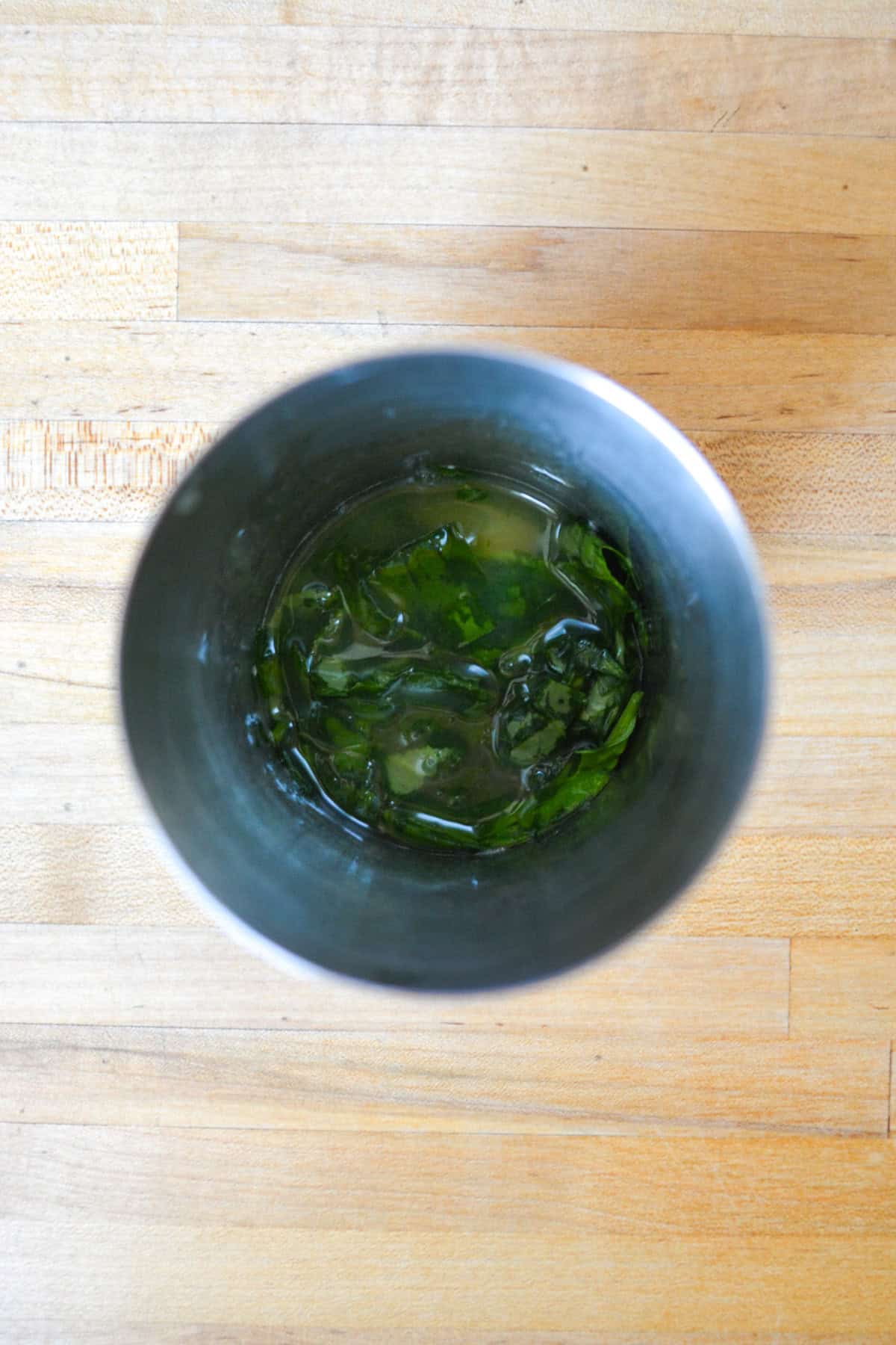 Muddles basil and lemon juice in a cocktail shaker.