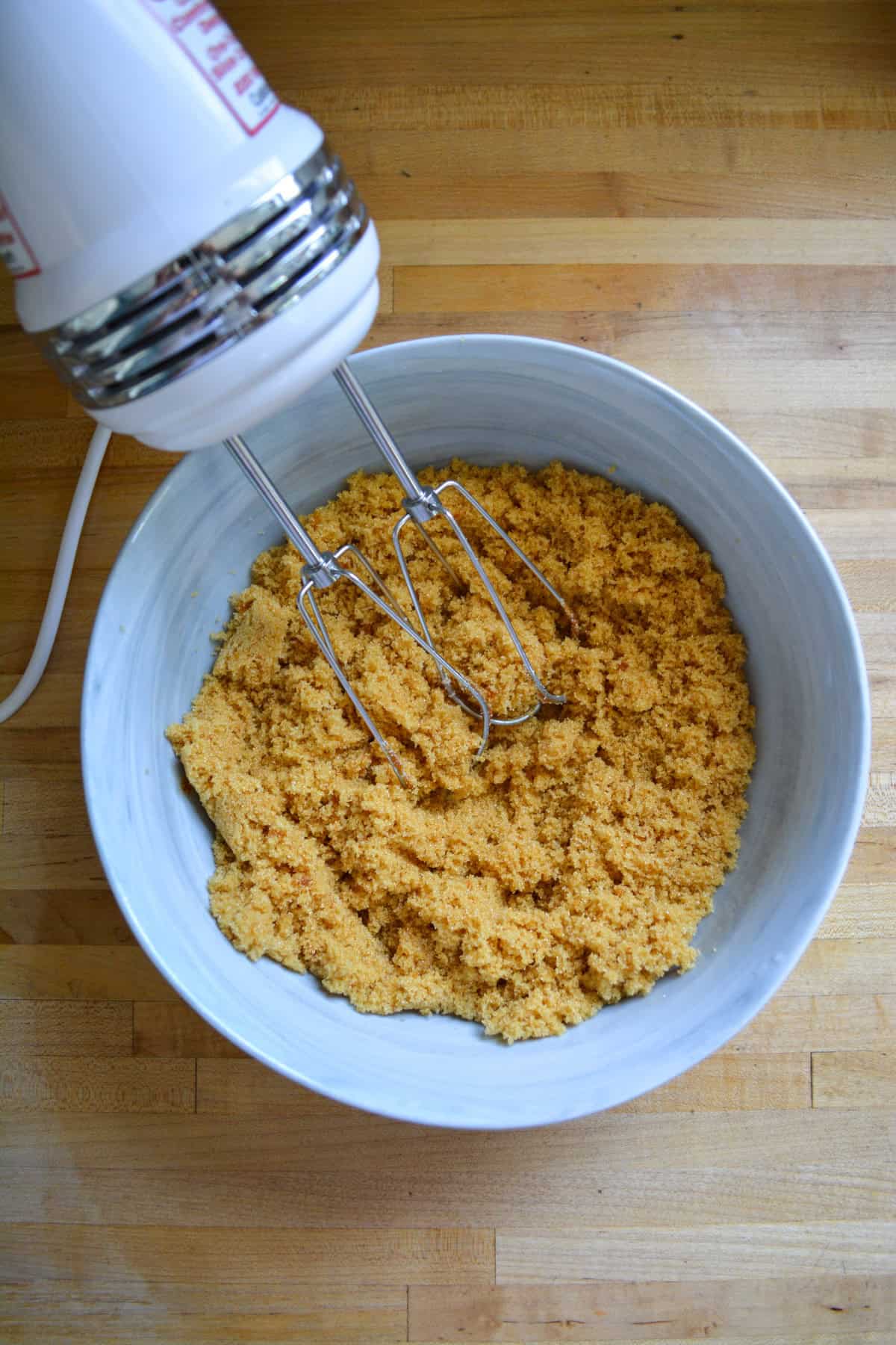 A hand mixer in a large mixing bowl of homemade brown sugar.