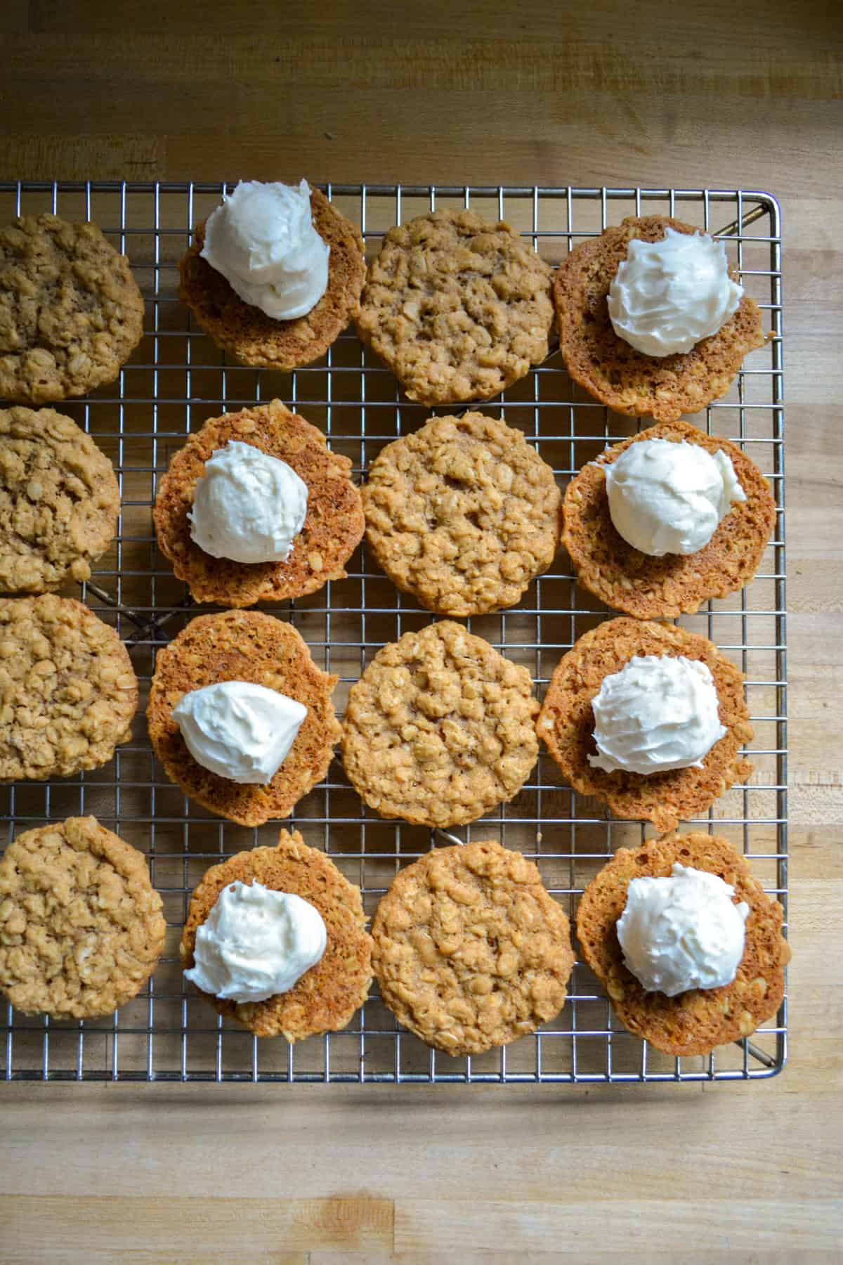 Cookies on a cooling rack being filled with frosting.