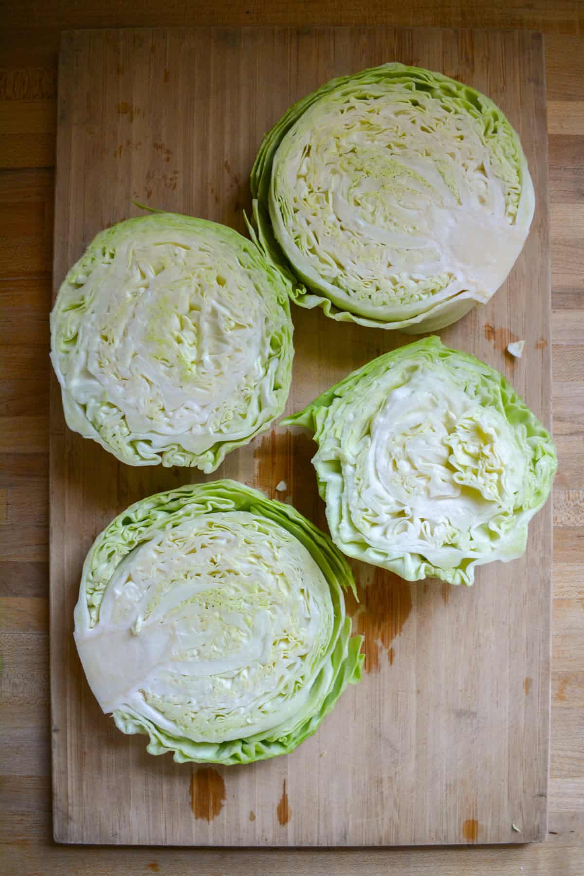 A head of cabbage cut in to slices on a wooden cutting board.