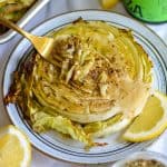 A fork piercing a roasted cabbage steak on a plate.
