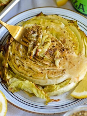 A fork piercing a roasted cabbage steak on a plate.