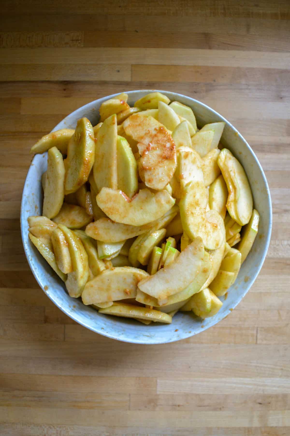 Sliced apples tossed with cinnamon and brown sugar in a large mixing bowl.