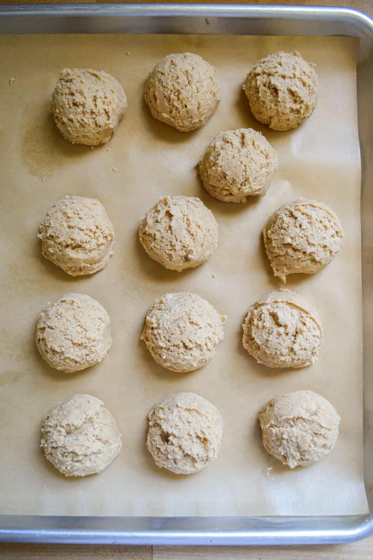 Scooped cookie dough on a parchment lined baking sheet.