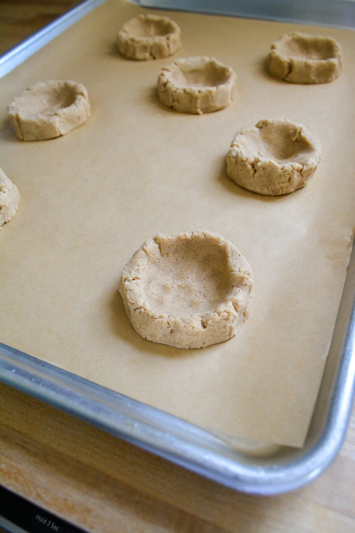 Cookie dough balls on a baking sheet with a well pressed into the center.