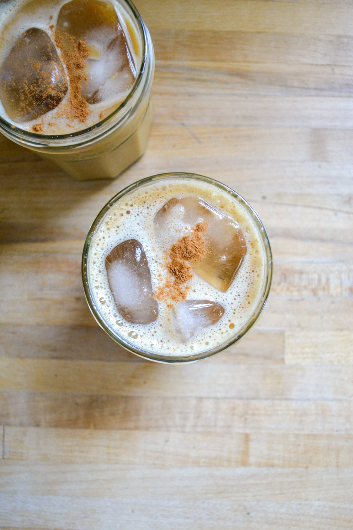 Oat milk and ice cubes added into the brown sugar latte glass topped with a sprinkle of cinnamon.