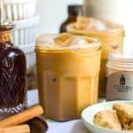 A glass of Brown Sugar Oat Milk Shaken Espresso nest to a bottle of brown sugar syrup.