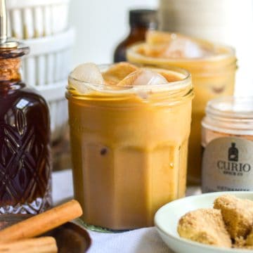 A glass of Brown Sugar Oat Milk Shaken Espresso nest to a bottle of brown sugar syrup.
