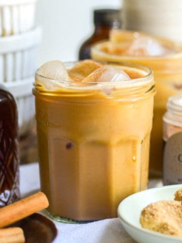 A glass of Brown Sugar Oat Milk Shaken Espresso nest to a bottle of brown sugar syrup.