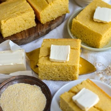 A square slice of vegan cornbread with butter on top on a cake server.