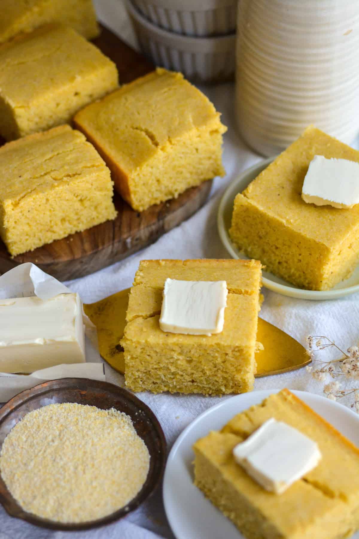 Slices of Vegan Cornbread on plates topped with pats of butter.