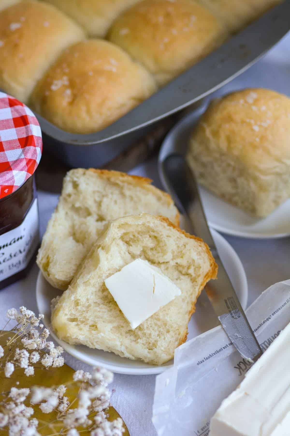A Vegan Dinner Roll cut in half with a pat of butter on it.