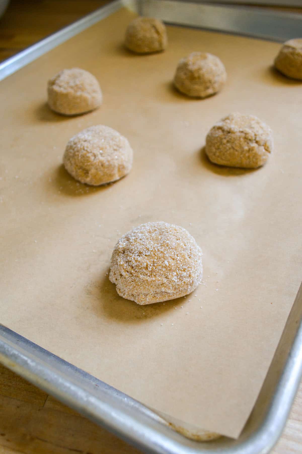 Vegan Molasses Ginger Cookie dough balls rolled in sugar on a baking sheet.