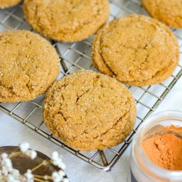 Chewy Vegan Molasses Ginger Cookies on a wire cooling rack next to a container of cinnamon.