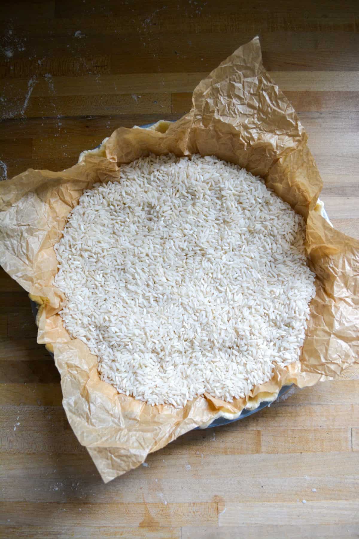 Parchment paper willed with rice added on top of the pie crust 