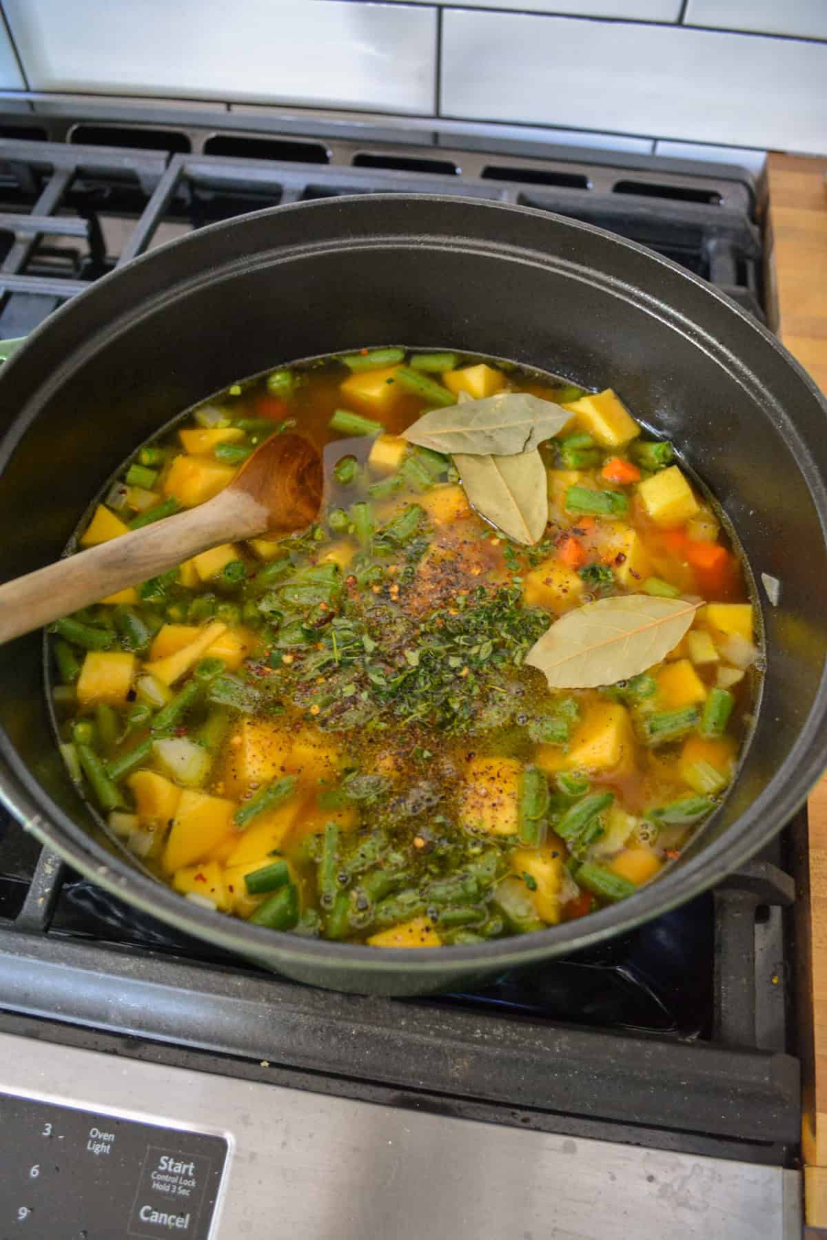 Vegetable stock, acorn squash, green beans and herbs added into the Dutch oven.