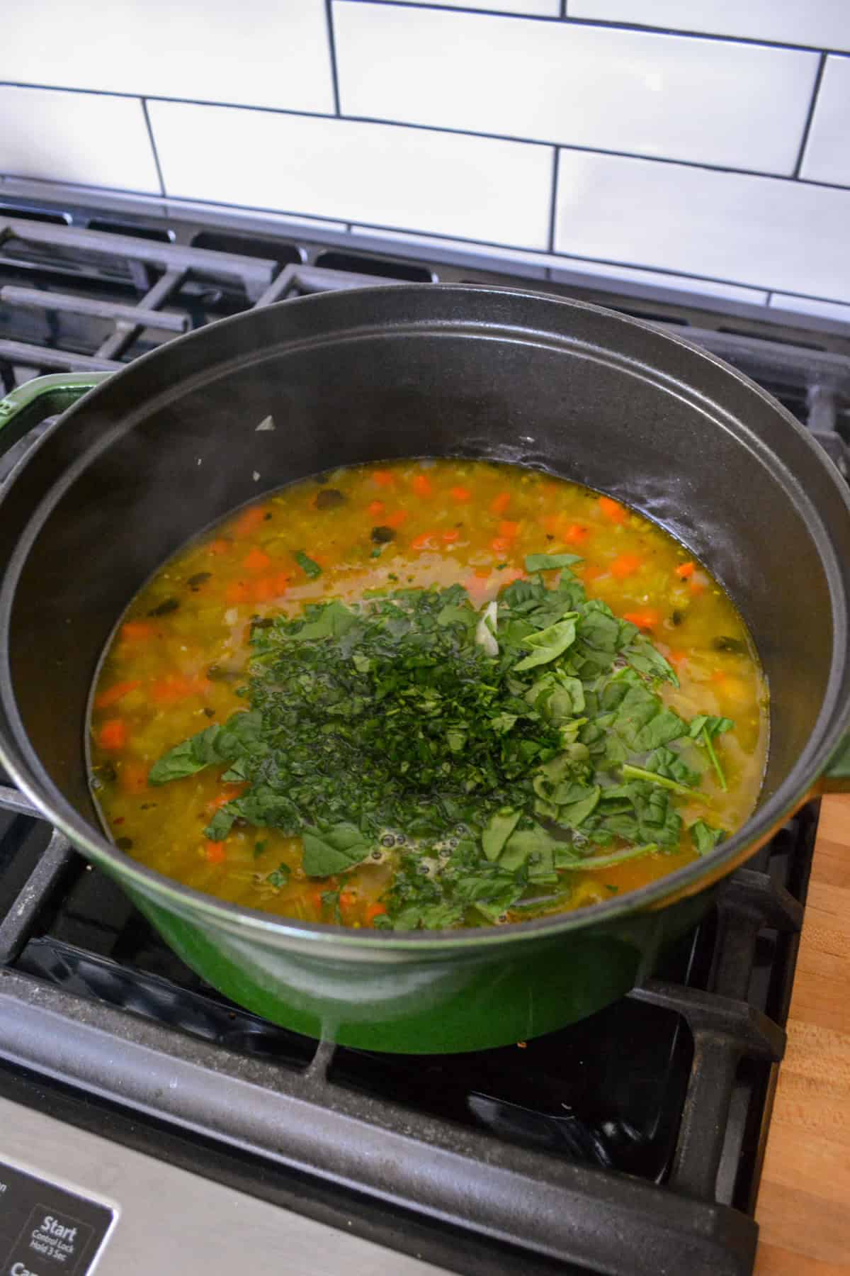 Adding chopped spinach and parsley to a simmering soup.