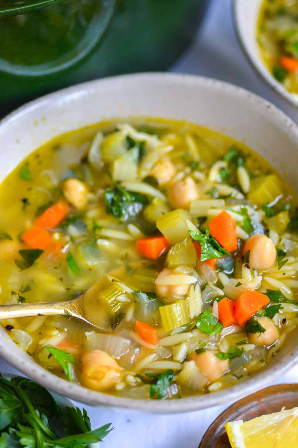 Vegan Lemon Vegetable Orzo Soup in a bowl with a gold spoon in it.