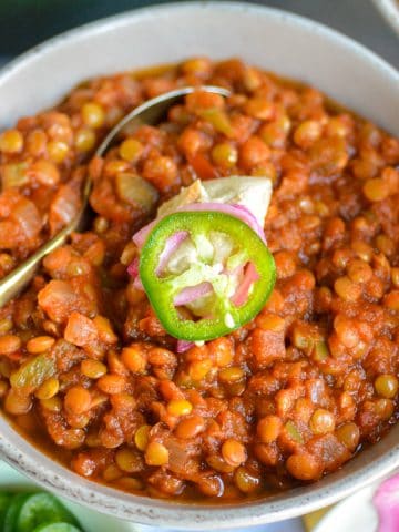 Lentil Chili in a bowl topped with sour cream and a jalapeno slice.