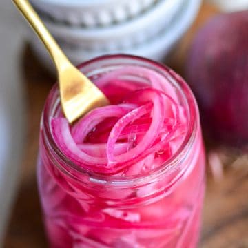 Quick Pickled Red Onions in a jar with a gold fork inside.