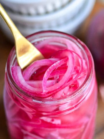 Quick Pickled Red Onions in a jar with a gold fork inside.