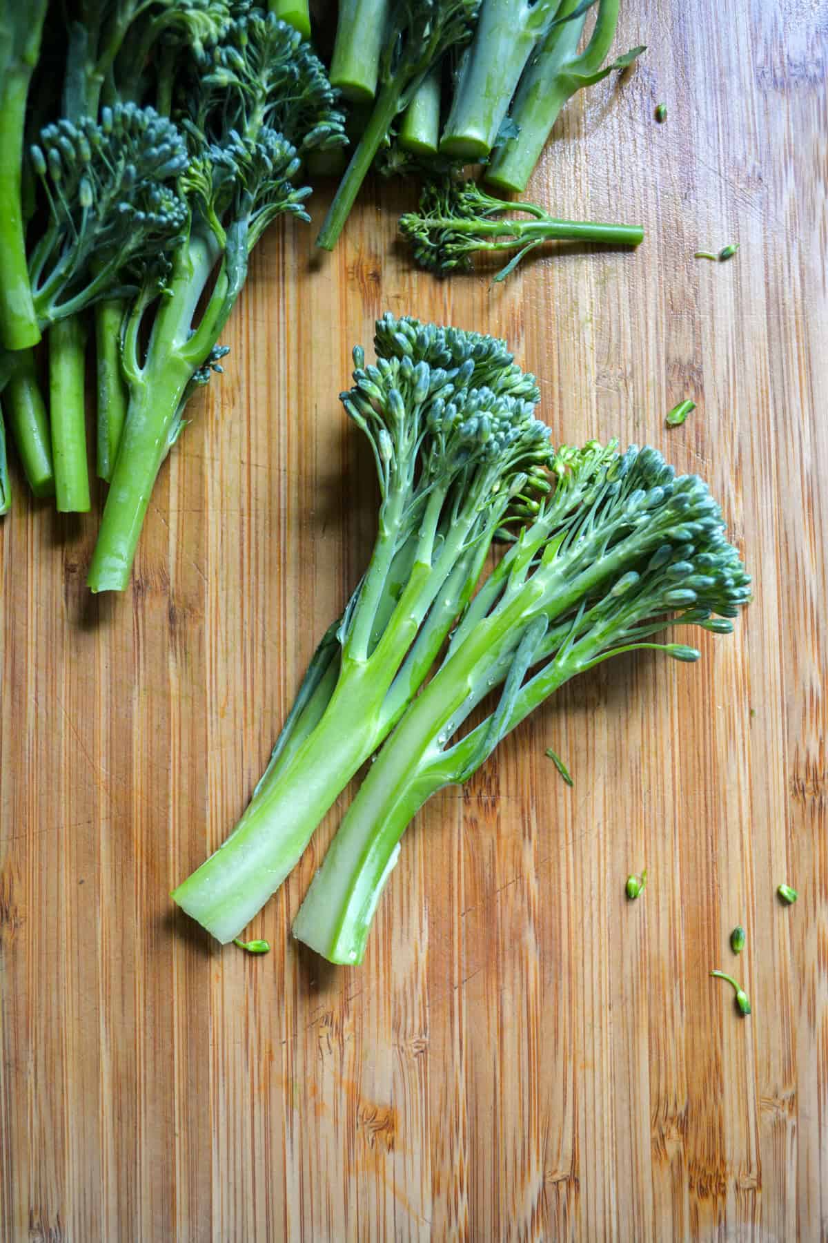 A broccolini split in half length wise on a wooden cutting board.