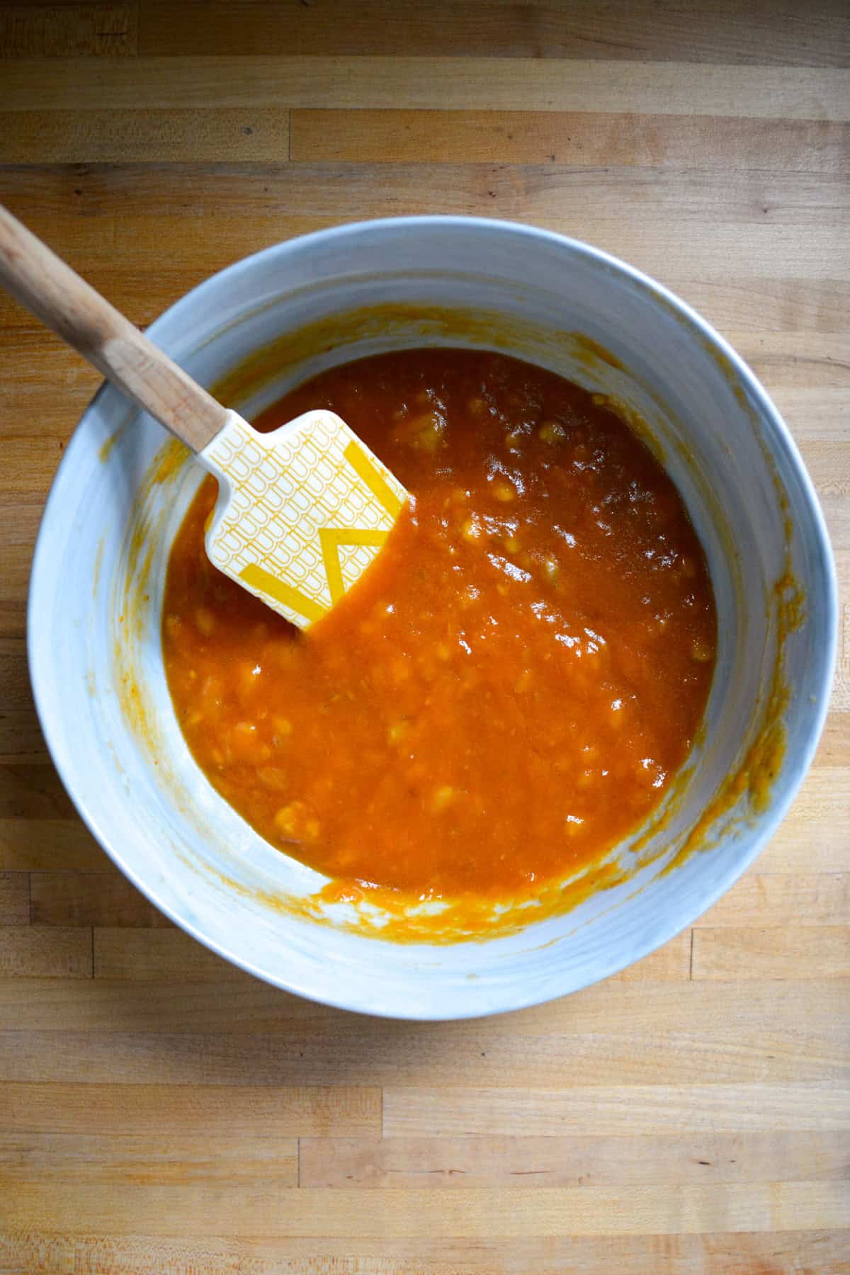Wet ingredients in a large mixing bowl with a rubber spatula inside.