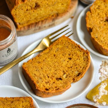 A slice of vegan banana pumpkin bread on a white plate with a gold fork.