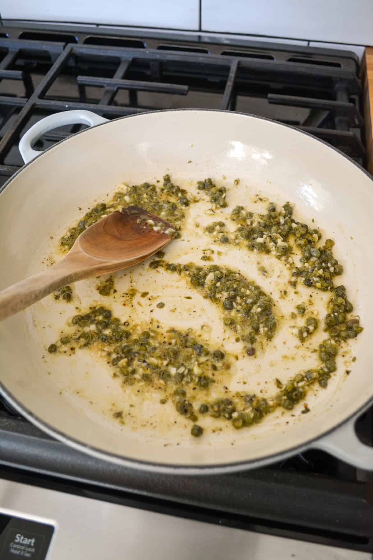 Sautéing garlic and capers in a large pan.
