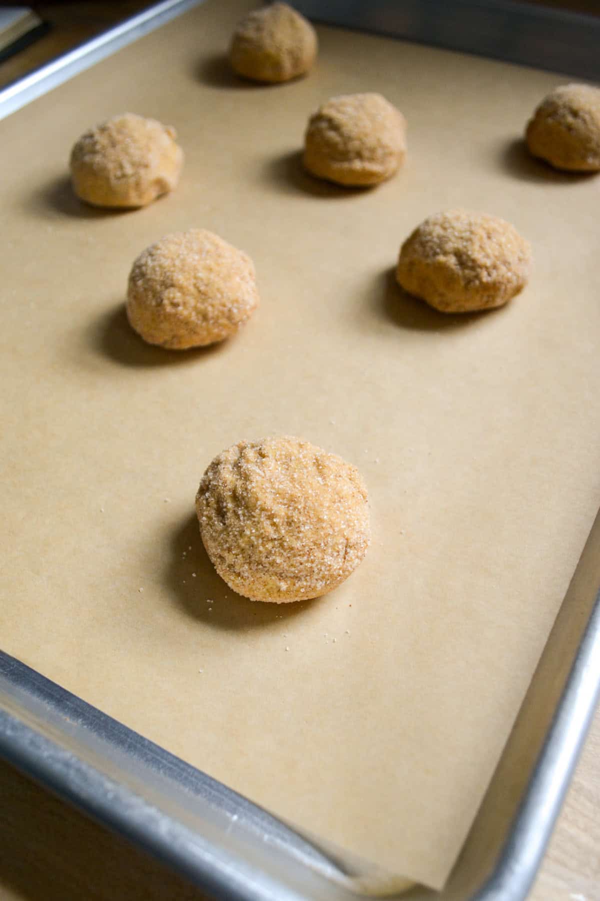 Pumpkin Snickerdoodle cookie dough balls on a lined baking sheet ready to bake.