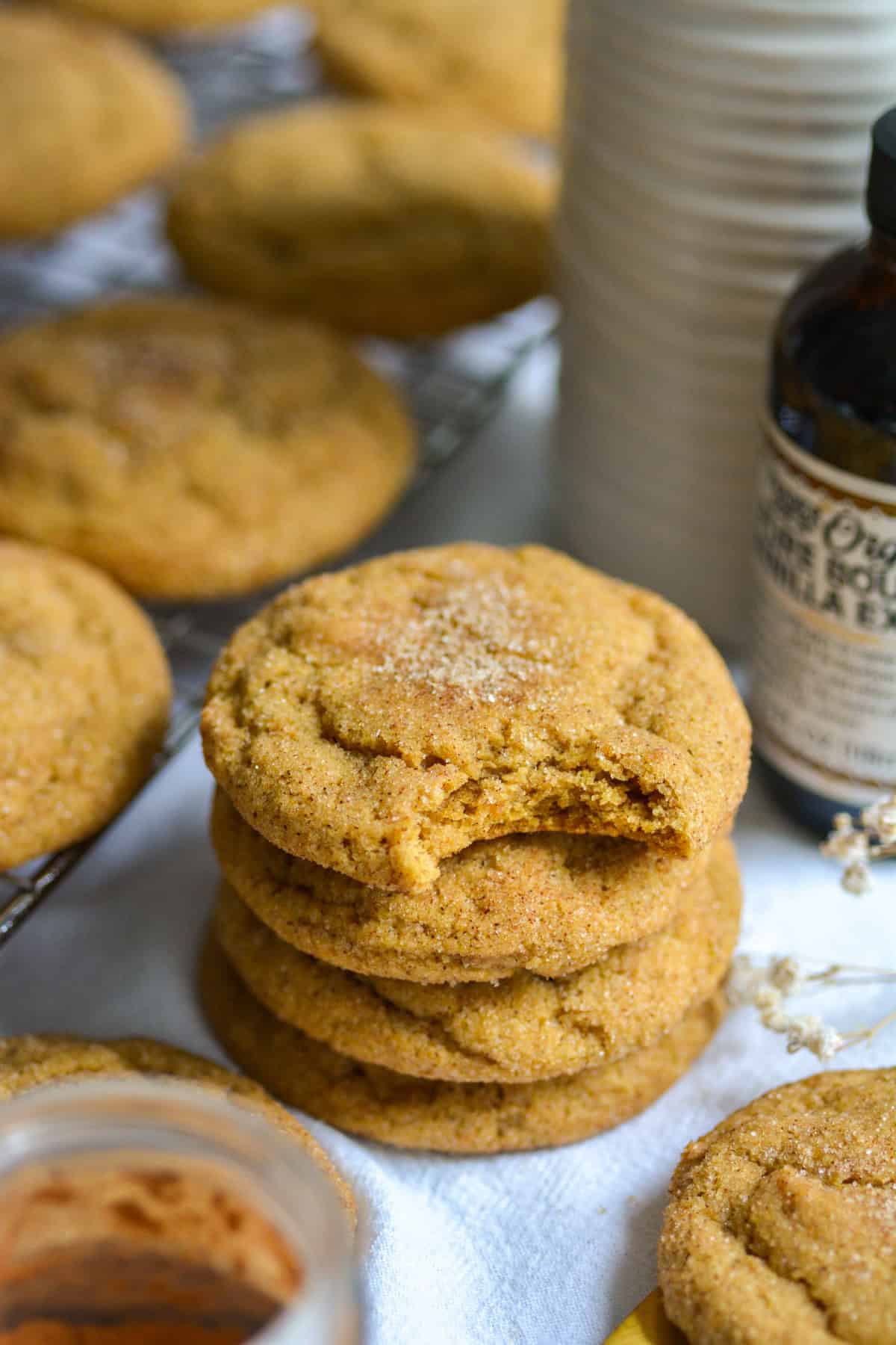 A Vegan Pumpkin Snickerdoodle on top of a stack of cookies with a bite taken out of it.