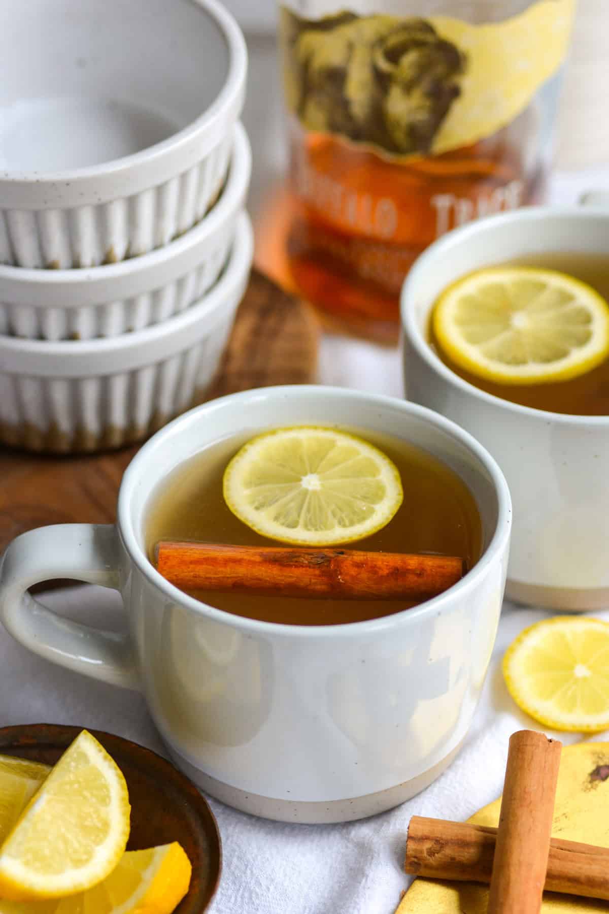 Two Bourbon Hot Toddys in mugs garnished with lemon wheels and cinnamon sticks.