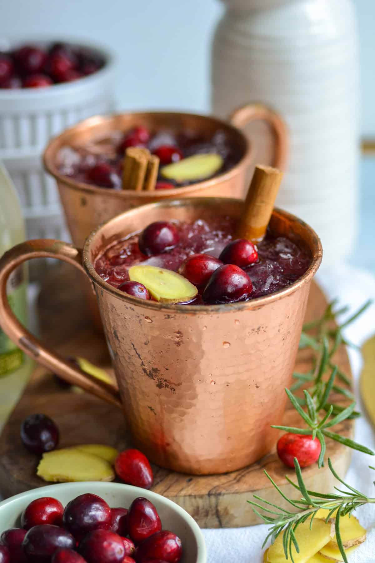 Two Cranberry Juice Cocktails in copper mugs topped with fresh cranberries.