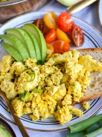 Tofu Scramble on a plate with a piece of toast and sliced avocado.