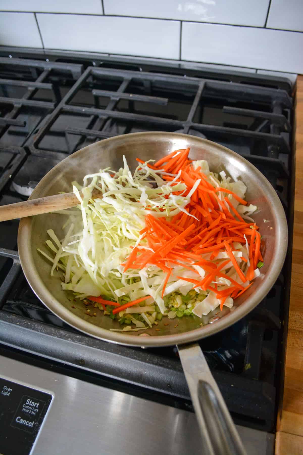 Cabbage and carrots added into aa skillet on a stovetop.
