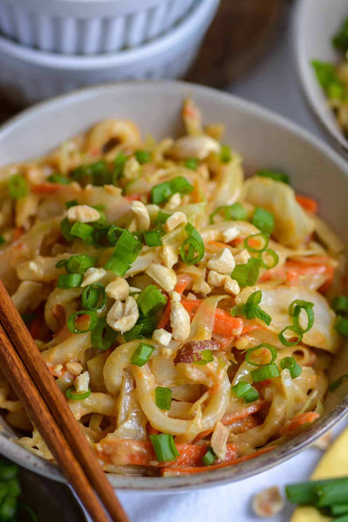 Vegan Peanut Udon Noodles in a bowl topped with green onions and crushed peanuts.
